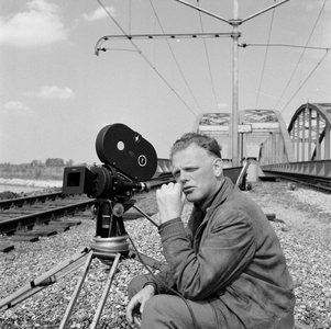 849530 Afbeelding van cineast Herman Wassenaar tijdens het filmen van treinen bij de spoorbrug over het ...